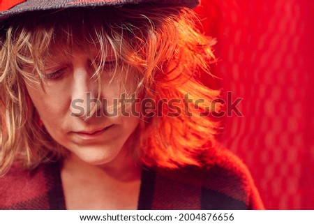 Portrait of serious sad middle-aged woman in hat on red background. Unprofessional female model in the Studio