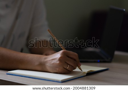 Female hand with a ring writes in a notebook with a pencil. Horizontal view.