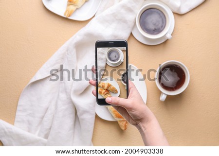 Female food photographer with mobile phone taking picture of tasty croissants with coffee, top view