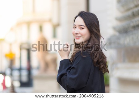 A picture of a beautiful long haired Asian female in a black robe walking and looking out in the city outdoors.