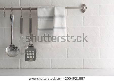 Soft kitchen towel and utensils hanging on rack near white brick wall Royalty-Free Stock Photo #2004921887
