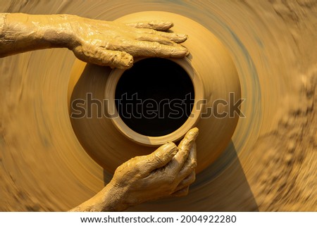 Muddy hands of a potter in focus while making a pot on a manual rotator. Royalty-Free Stock Photo #2004922280
