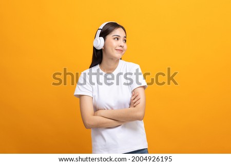 Cheerful asian female teenager listen to the music with white headphone dancing on isolated yellow background. Beautiful young woman in hand touch a wireless headphone having fun with music.