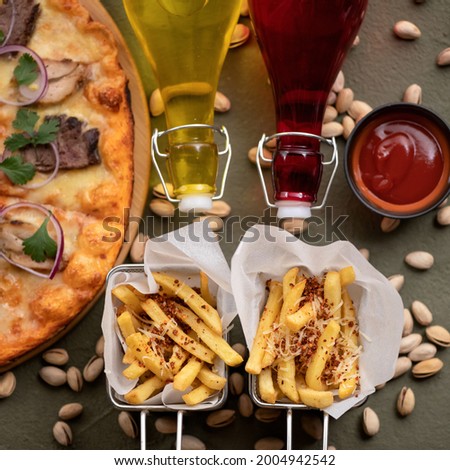 Delicious Italian food on table. Pizza, French fries, oil or wine bottles, ketchup and pistachios on it. Flat lay or top view. Soft focus.