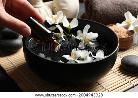 Woman dripping jasmine essential oil into bowl on table, closeup
