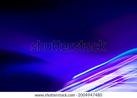 Abstract colorful background with  white , purple and blue glowing lines of different thickness and curvature from city lights on a black background. The blur is intentional.