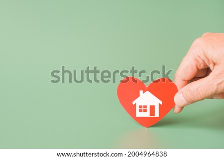 hand holding red heart with home sign on green background for family home, homeless shelter and real estate, housing and mortgage crisis, foster home care, family day care concept
