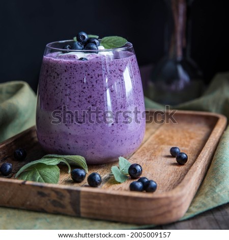 Blueberry smoothie on a wooden salver and black background .  Bilberry smoothie low key . Whortleberry smoothie on a  wooden table.  Very peri Royalty-Free Stock Photo #2005009157