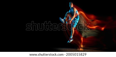High jump with ball. Young caucasian male basketball player playing basketball isolated over dark studio background in mixed light. Concept of motion, power, speed, healthy lifestyle, professional