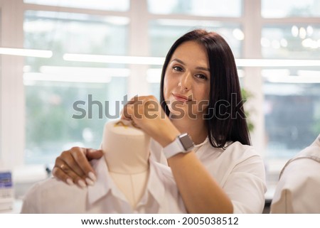Portrait of happy casual seamstress posing with mannequin at modern sewing workshop medium closeup. Happy adorable tailor dressmaking business owner standing with dummy at design studio