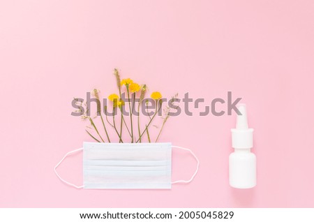 A set of wild flowers and herbs under a disposable protective mask and a mock-up of nasal spray on a light pink background. The concept of means of protection and treatment of seasonal allergies. 