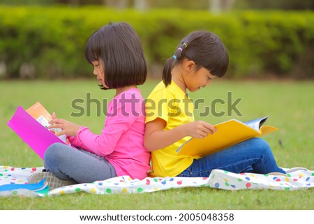 Cute little girl  reading books on the grass. She has a look of enjoyment on her face and she looks very relaxed. Which increases the development and enhances learning skills outside the room.