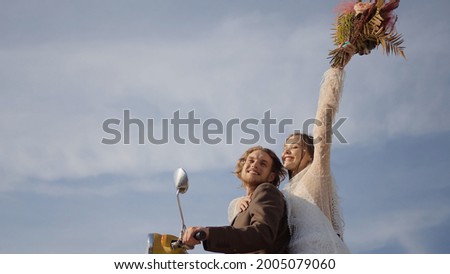 Beautiful couple of newlyweds on scooter. Action. Young newlyweds in stylish wedding dresses on scooter. Newlyweds went on motorcycle trip. Wedding photo shoot on scooter Royalty-Free Stock Photo #2005079060