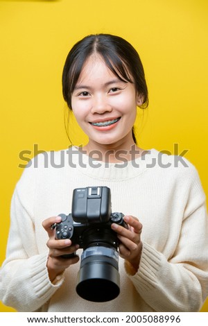 Portrait of a surprise girl with a camera in hand on a yellow background. Isolated studio. 