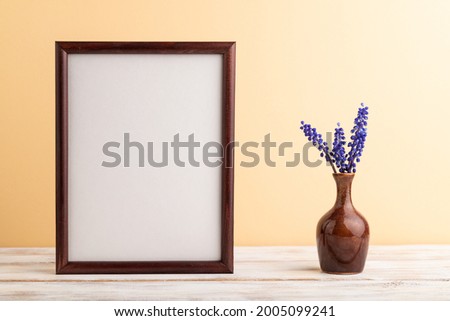 Wooden frame with blue muscari hyacinth flowers in ceramic vase on orange pastel background. side view, copy space, still life, mockup, template, spring, summer minimalism concept.