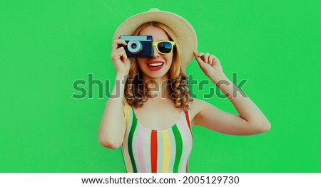 Summer portrait of happy smiling young woman with retro camera wearing a straw hat on green background