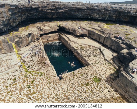 Aerial drone view on famous Poll na bPéist - The Wormhole, Inishmore, Aran islands, county Galway, Ireland. Popular tourist hike and landmark, Warm sunny day. Tourist swimming inside nature pool Royalty-Free Stock Photo #2005134812