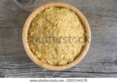 Nutritional yeast flakes in small bamboo bowl on textured wooden surface. Highly nutritious and healthy food, ideal for vegan recipes. Top center view with natural light. Royalty-Free Stock Photo #2005146578