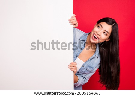 Portrait of attractive cheerful curious girl holding big blank poster ad promo isolated over bright red color background Royalty-Free Stock Photo #2005154363