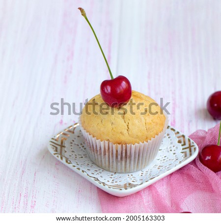 homemade fresh muffin decorated with fresh cherries stands on a saucer on a wooden background. Cherry muffin close-up. Cherry with a root lies on a cupcake. High quality photo