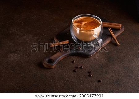 Hot and aromatic coffee spilling from glass cup on the dark background. Concept of tasty refreshment beverage with coffee. Copy space for text, menu or recipe