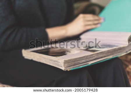 Close-up of a girl in dark clothes sitting on the sofa, holding an album on her lap and looking at old photos
