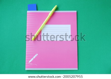 Pink notebook with stationery accessories on a green background. 1 September is the day of knowledge.