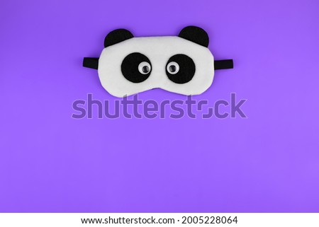 Sleep mask with a panda face. Cute sleep mask on a purple background, top view. Accessories for sleeping and relaxing