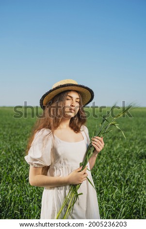 girl in a straw hat and a sundress against the background of a green field and a clear blue sky