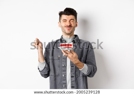 Happy birthday guy making wish on cake with candle, celebrating bday, standing on white background