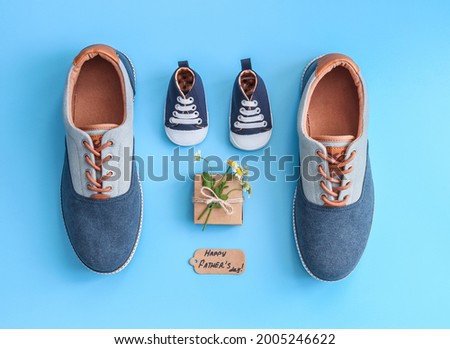 A pair of men and a baby sneakers with daisies and a gift lie on a blue background, top view close-up.
