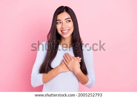 Photo portrait of girl smiling thankfully keeping hands on heart looking copyspace isolated on pastel pink color background