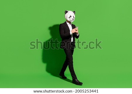 Photo of traveler china blogger walk hold telephone wear panda mask black tux shoes isolated on green color background