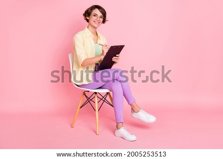 Photo of charming cute young woman wear yellow shirt glasses sitting chair signing documents isolated pink color background