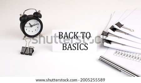 Card with text BACK TO BASICS on a white background, near office supplies and alarm clock. Business