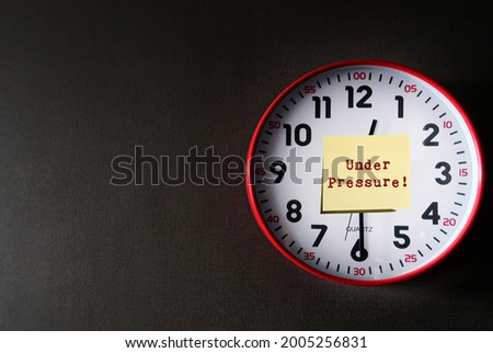 Clock on dark gray copy space background with note written UNDER PRESSURE! means dealing with time constraints which are often outside of control - difficulty task or having insufficient knowledge Royalty-Free Stock Photo #2005256831