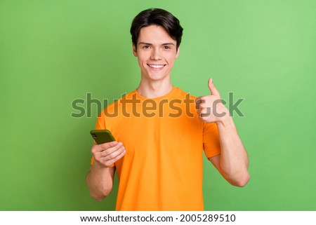 Photo of positive happy young man hold hand phone make thumb up advert isolated on green color background