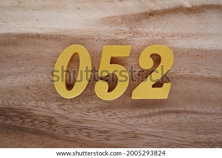 Gold Arabic numerals 052 on a dark brown to off-white wood pattern background.