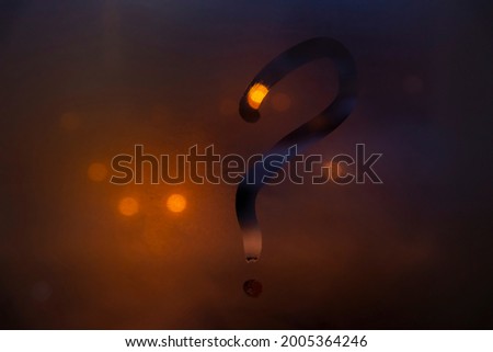 Close-up view of question mark drawing by finger on glass misted window. Orange blurred night background. Bokeh light. Selective focus. No people. Question and answer theme.