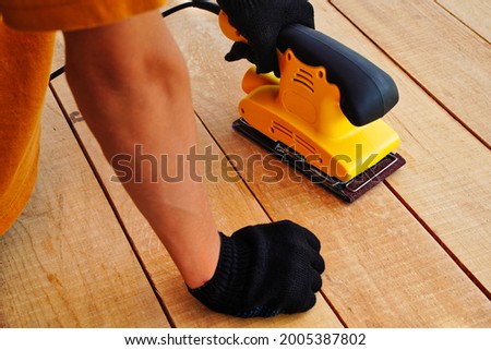 Manual electric yellow grinder. Wooden surface for processing. Working with wood, polishing surfaces by a carpenter Royalty-Free Stock Photo #2005387802
