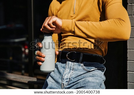 Man in a yellow long sleeve top opening a gray stainless steel tumbler bottle mockup