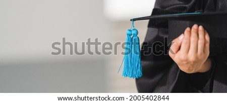 Close-up shot of a university graduate in graduation gown holding a degree certification with mortarboard to shows and celebrates success in the college commencement day. Education stock photo