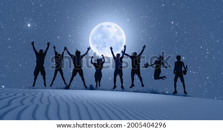 Group of friends jumping on top of dune with arms raised in air with full blue moon "Elements of this image furnished by NASA "