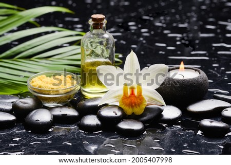 Spa still life of with 
White orchid , candle ,green palm leaves,salt in bowl, oil bottle  and zen black stones on wet background
