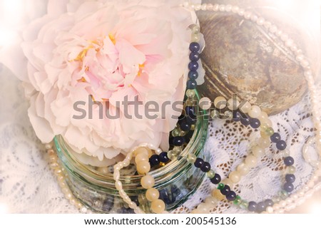 Vintage background with pink peony, jewels in glass jar and old rusty iron ball on the lace. Light glow.
