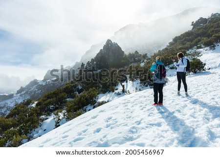 Rear view of two women taking pictures to the mountains in Pico Ruivo footpath covered with snow in Madeira island