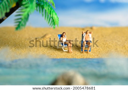 Miniature people toy figure photography. Men and girl couple relaxing on beach chair when daylight at seaside. Image photo