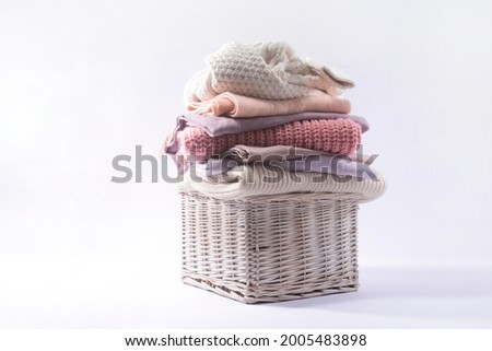 Stack of different warm sweaters in basket isolated on white background 

