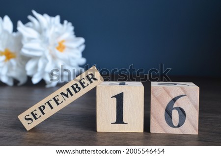 September 16, Date cover design with calendar cube and white Paeonia flower on wooden table and blue background.