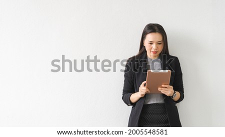 Portrait of a cheerful confident Asian businesswoman in a business suit holding and using a digital tablet in the business building. Business stock photo